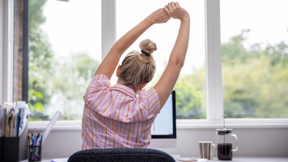 A woman stretching in front of a computer 