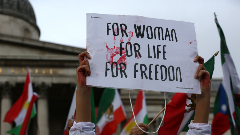 women holding protest banner reading "woman life freedom" 