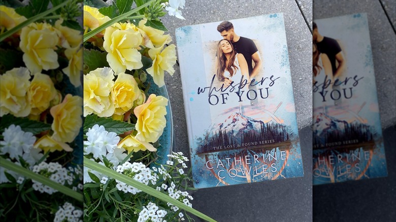 Physical copy of Whispers of You next to flowers