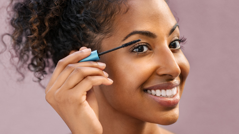 Woman smiling while applying mascara 