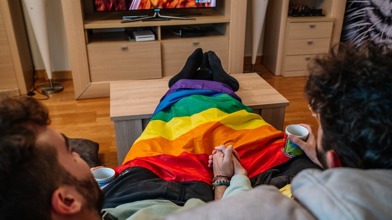 Gay couple watching TV wrapped in a pride flag