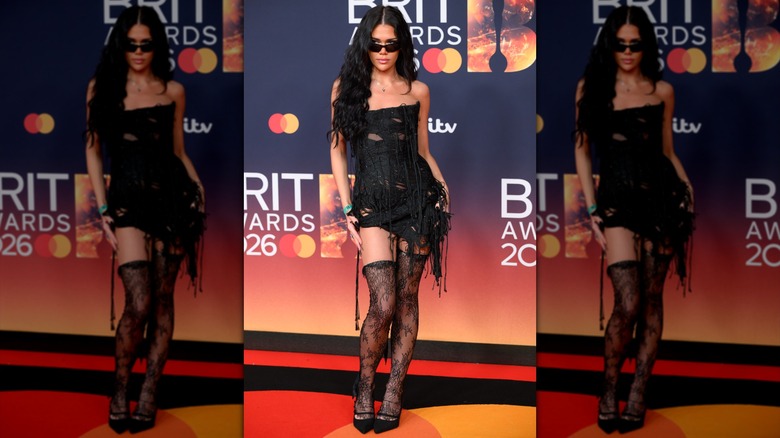 Flossie posing in black thigh-high lace stockings and a shredded black minidress with strings hanging on it.