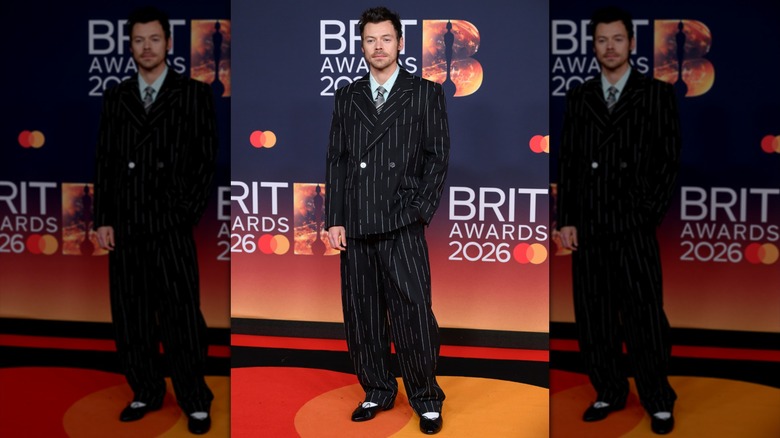 Harry Styles posing in a baggy black pinstripe suit.