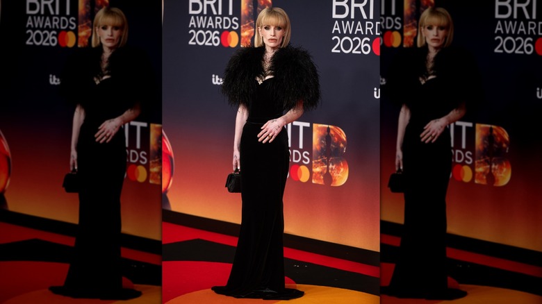 Kelly Osbourne posing in a floor-length black velvet gown with feathers on the shoulders.