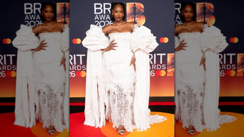 Tems posing in a strapless white lace dress with detached puffy sleeves and floor-skimming fringe.