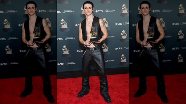 Yungblood posing in a black leather best and pants while holding a Grammy