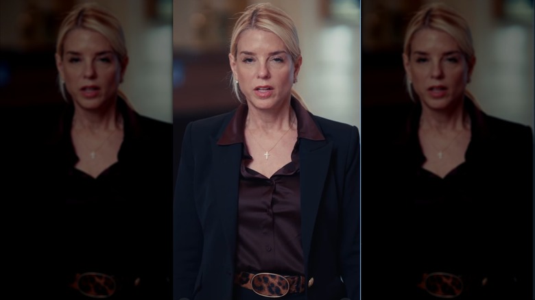 Pam Bondi speaking while wearing a brown shirt and black jacket with a leopard pattern belt.