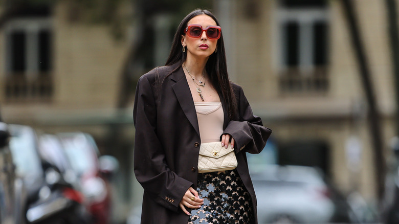 Gabriella Berdugo wears an oversized blazer, a Chanel quilted belt bag, a crop top, a sequin skirt, and Nike Air sneakers in Paris, France