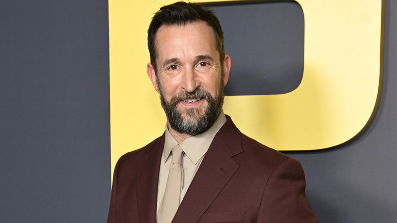 Noah Wyle smiling while attending an event in a brown suit with a tan tie and matching shirt