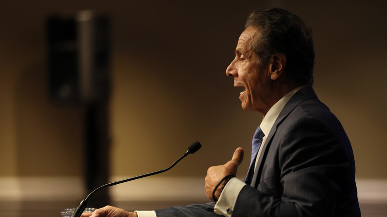 Andrew Cuomo talking into a microphone, case in dark light.