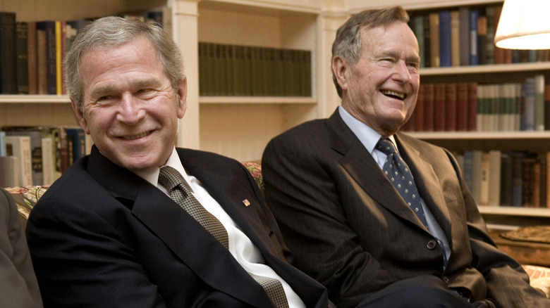 George W. Bush and George H. W. Bush sharing a laugh while wearing suits