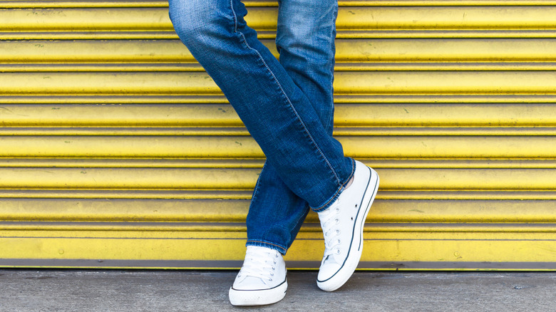 Woman wearing jeans and sneakers posing against a garage door.