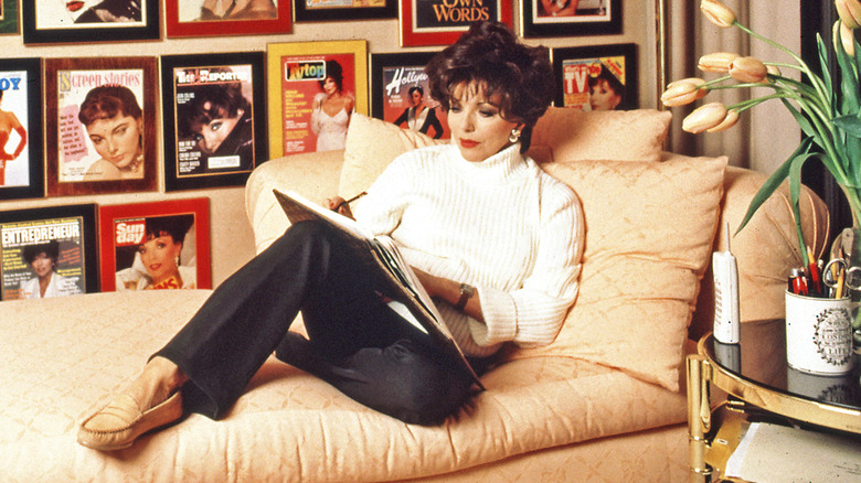 Joan Collins lounging on a settee while working on something in 1995