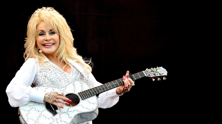 Dolly Parton in a bejeweled white outfit holding a white guitar
