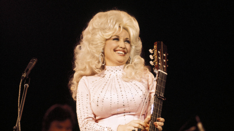 Dolly Parton in long blonde hair wearing a pink rhinestone-studded outfit