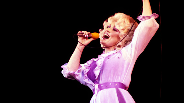 Dolly Parton singing in a purple outfit with short golden hair