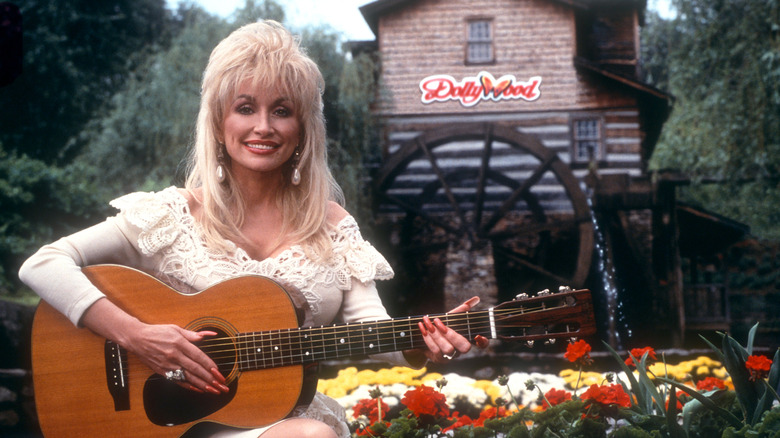 Dolly Parton and her guitar with Dollywood in the background