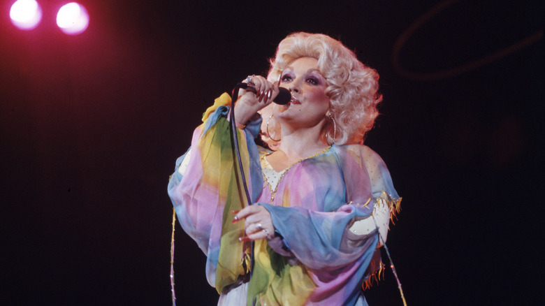 Dolly Parton singing in a soft-pleated colorful outfit with short golden hair