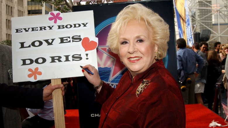 Doris Roberts signing a sign that says "Everybody Loves Doris"