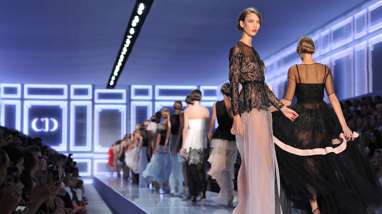 Karlie Kloss posing at the end of a fashion runway as other models walk around her