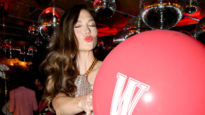 Karlie Kloss pouting at the camera and holding a red balloon with a white "W" on it