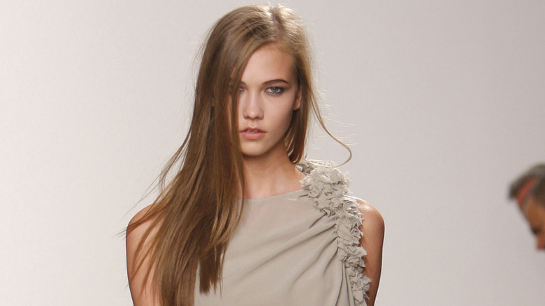 A young Karlie Kloss walking on a fashion runway against a white backdrop