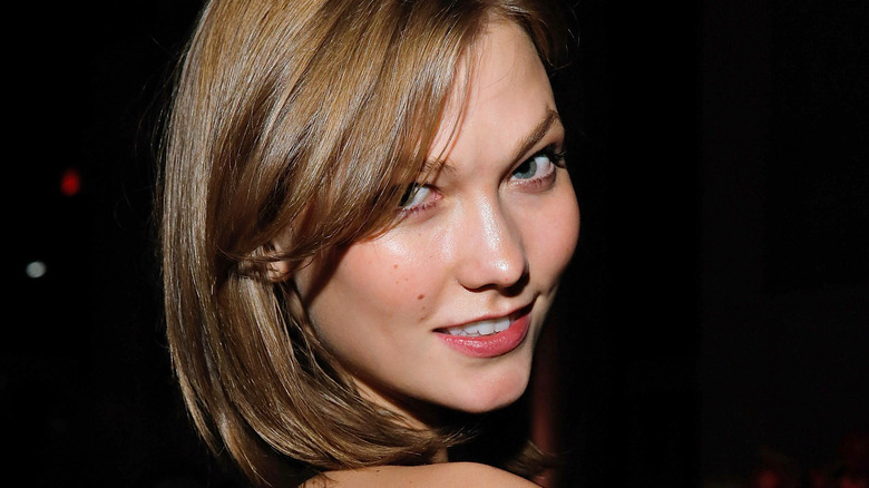 A close up image of Karlie Kloss looking at a camera against a black backdrop