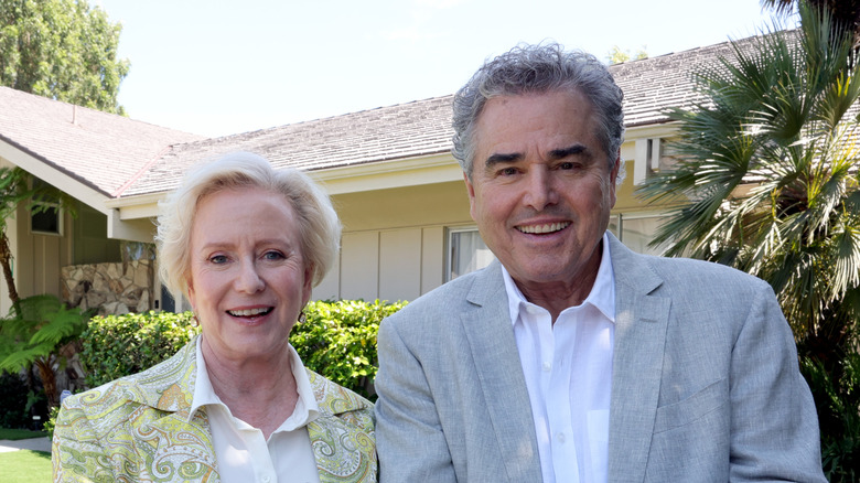 Christopher Knight and Eve Plumb smiling while posing with a plaque in front of the Brady Bunch house