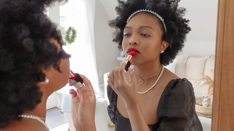 Woman applying red lipstick in an LBD