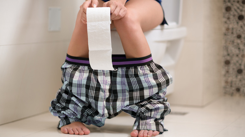 person sitting toilet holding toilet paper