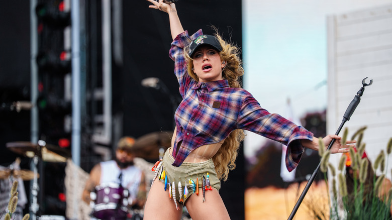 Slayyyter in a flannel corset top, and hot pants fitted with fishing lures
