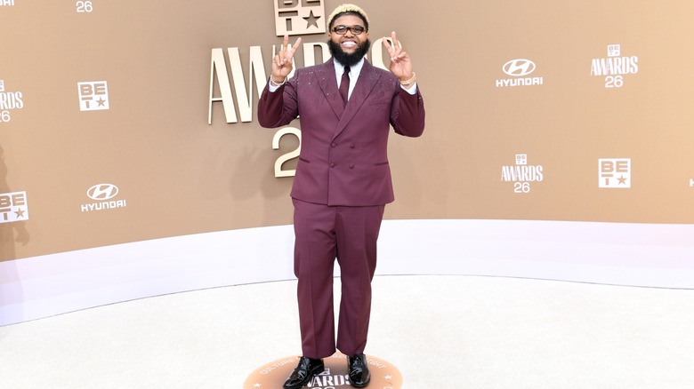 Druski making peace signs to the camera, while wearing a purple suit, on the red carpet at the 2026 BET Awards