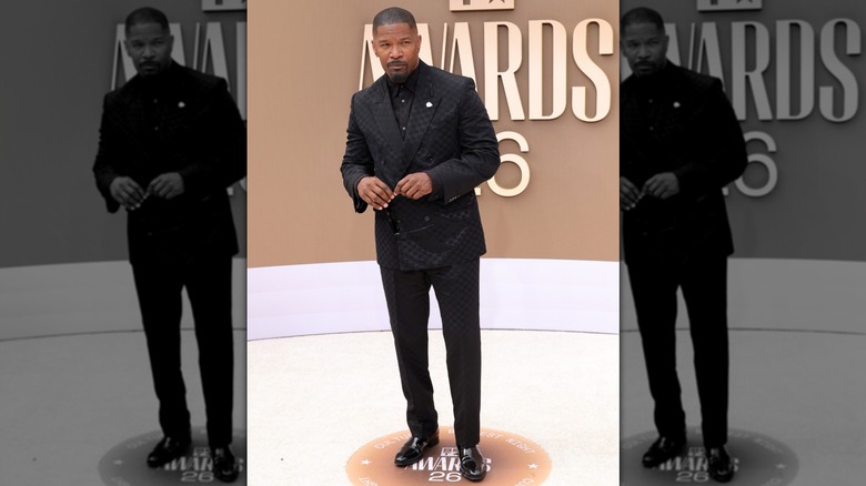 Jamie Foxx in an all black suit and holding a pair of sunglasses on the 2026 BET Awards red carpet