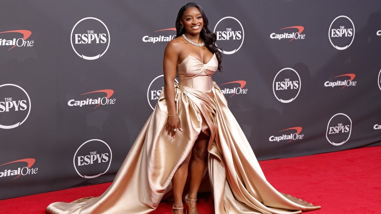 Simone Biles in a long champagne-gold dress, smiling, on the 2026 ESPYs red carpet