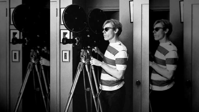 Andy Warhol operating a film camera in a striped shirt.