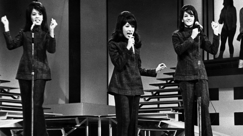 The Ronettes performing onstage in the 60s, all wearing matching two-piece outfits.