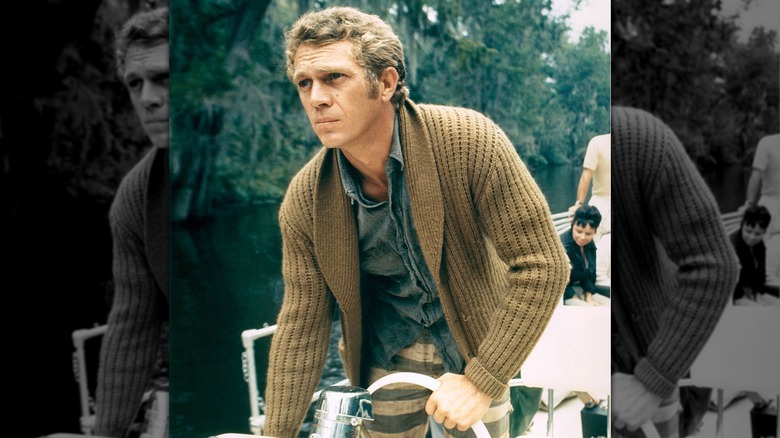 Steve McQueen behind the wheel of a boat in a chunky cardigan, circa 1965.