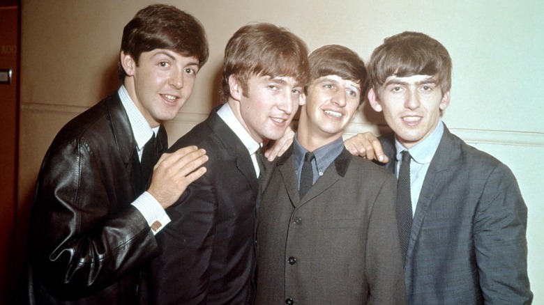 The Beatles shoulder to shoulder, in 1963, all wearing suits and smiling.