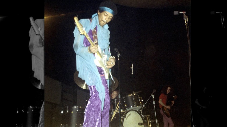 Jimi Hendrix playing his guitar onstage in the late '60s, wearing purple velvet bell bottoms.