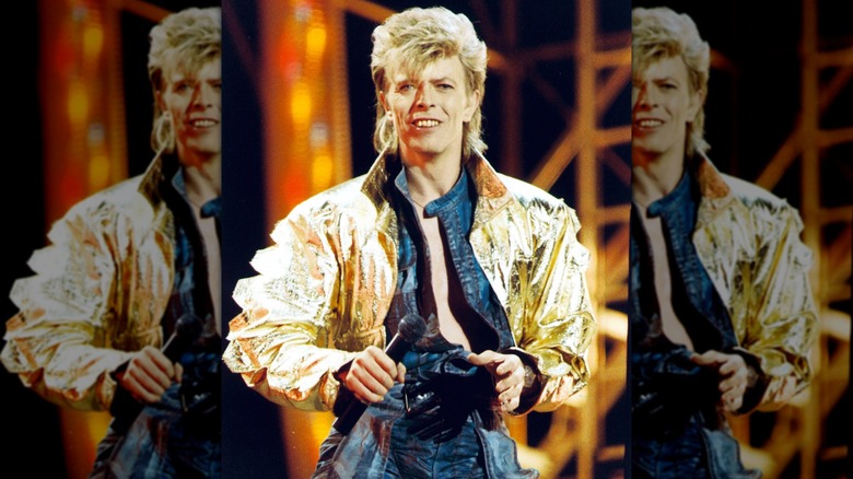 David Bowie on tour in the 1980s, wearing a open-chest blue one-piece with a gold jacket.
