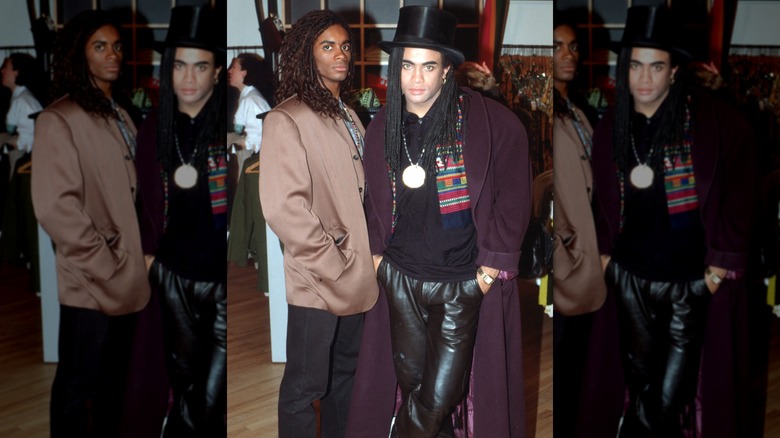 Fab Morvan (left) and Rob Pilatus (right) of Milli Vanilli at an event in 1989; Morvan wearing a tan jacket with black pants, Pilatus wearing a heavily accessoried black outfit with burgundy jacket and black hat.