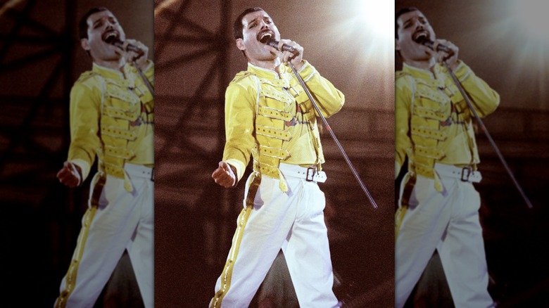 Freddie Mercury performing in the 1980s, wearing a yellow jacket and white pants.