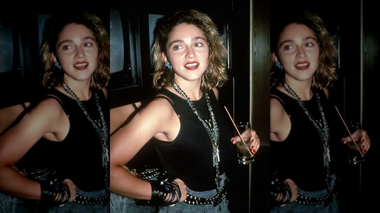Madonna smiling in 1985 while wearing a sleeveless black shirt, jeans, and heavy accessories.