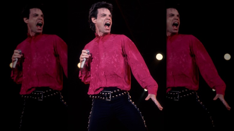 Mick Jagger performing onstage in 1989, wearing a hot pink lace shirt and studded black pants.