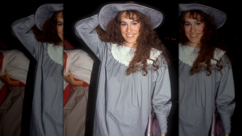 Sarah Jessica Parker smiling in the 1980s, wearing a oversized gray dress and matching gray hat.