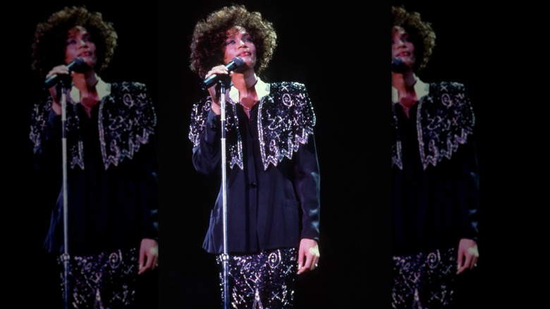 Whitney Houston performing in 1987, wearing a black patterned shirt and skirt set.