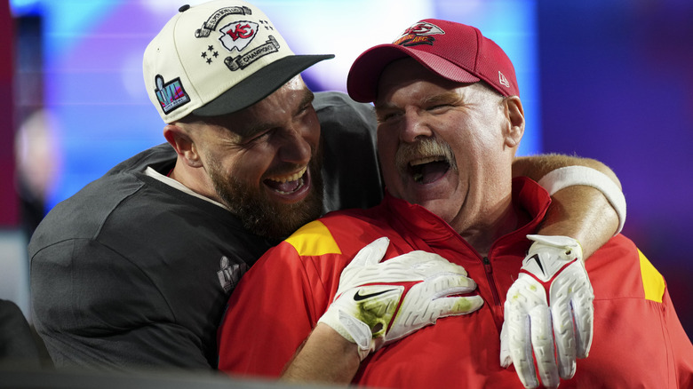 Travis Kelce embracing and laughing with Andy Reid on a football field.