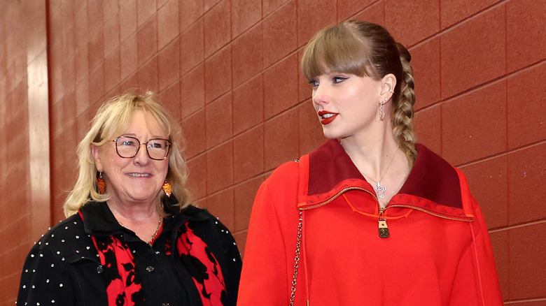 Donna Kelce and Taylor Swift walking together beside a red tiled wall.