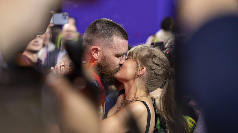 Travis Kelce and Taylor Swift kissing amid a crowd of people.