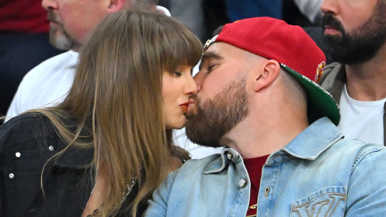 Taylor Swift and Travis Kelce kissing at a sporting event.